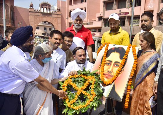 A group of people lay a large marigold wreath before a garlanded framed portrait of Madan Lal Dhingra on a street in Amritsar.